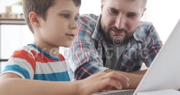 男孩在家里和父亲一起学习使用笔记本电脑视频的预览图
