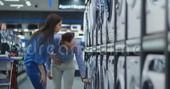 年轻的已婚夫妇男女在休闲服装电器商店选择买洗衣机回家打开门视频的预览图