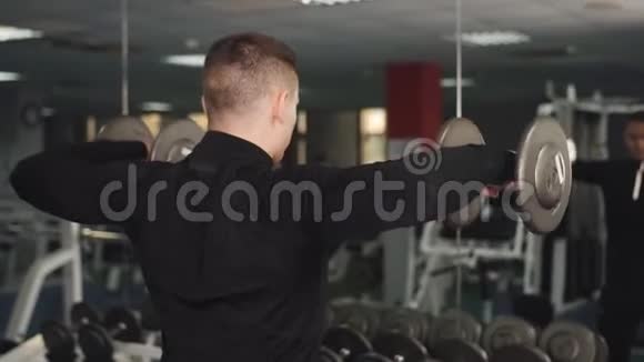 一个人用哑铃训练他的二头肌并在镜子里看他的身体视频的预览图