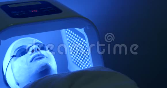 这位带着面具和眼镜的轻松女人正在接受面部的LED光疗法水疗沙龙的位置4K录像视频的预览图