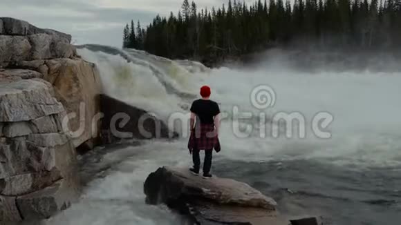 清晨旅行者站在挪威森林瀑布前穿着红帽子视频的预览图