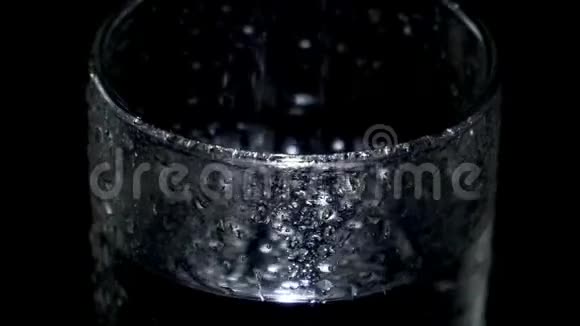 一杯湿玻璃杯里的水在黑暗中旋转光线在水滴中闪烁视频的预览图