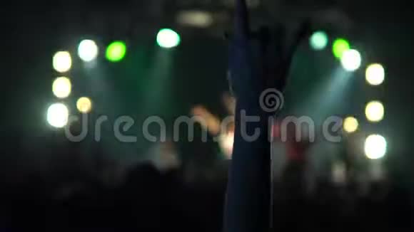 一个音乐音乐会上的女人举起了手一群欢笑的人站在鲜艳的舞台灯光前剪影式视频的预览图