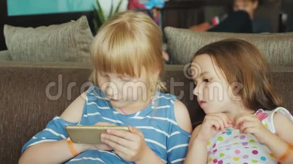 小妹妹们在沙发上休息在瑞瑟平纳的一家旅游旅馆里玩游戏视频的预览图