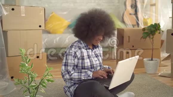 非洲女性有非洲发型坐在地板上使用笔记本电脑移动的概念视频的预览图