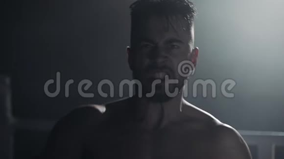 戴着拳击手套的愤怒男子在站在拳击台上的镜头前情绪化地尖叫慢动作视频的预览图