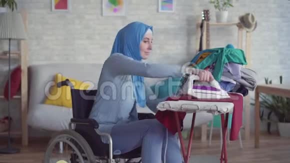 美丽的穆斯林妇女坐轮椅做作业熨衣服视频的预览图
