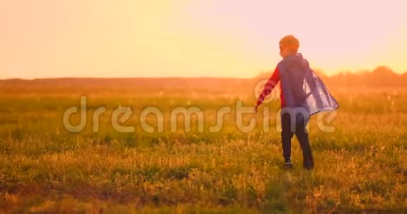 日落时分一个穿着超级英雄服装的男孩笑着跑过田野视频的预览图