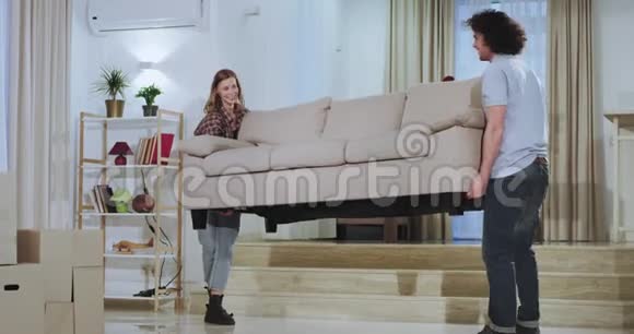 为一对年轻漂亮的夫妇搬家一天他们拿着大沙发在生活中非常兴奋地摔倒在地上视频的预览图