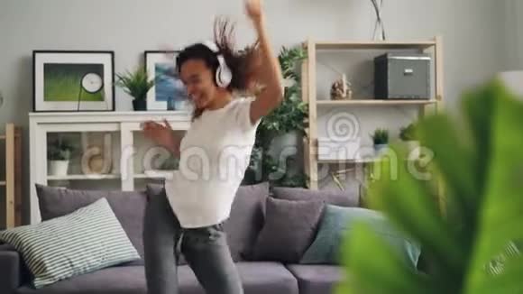 免费的年轻女士非裔美国学生在家里玩得很开心用无线方式跳舞唱歌听音乐视频的预览图
