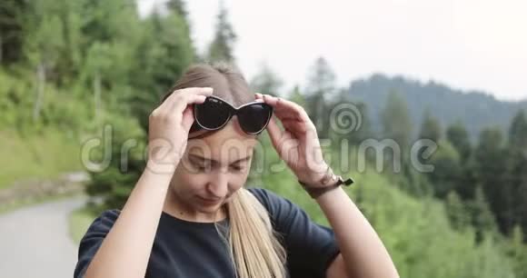 一个戴太阳镜的女人在绿树成荫的群山背景下的肖像视频的预览图