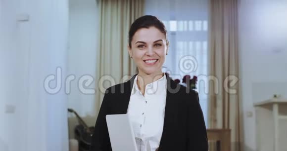 在镜头前一位穿着西装笑容满面长着白牙手里拿着一个漂亮女商人的画像视频的预览图
