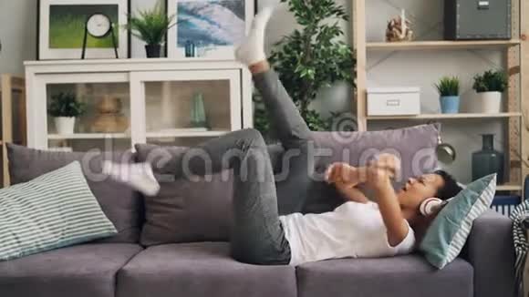 漂亮的年轻女士非洲裔美国潮人正在家中的沙发上唱歌跳舞听音乐视频的预览图