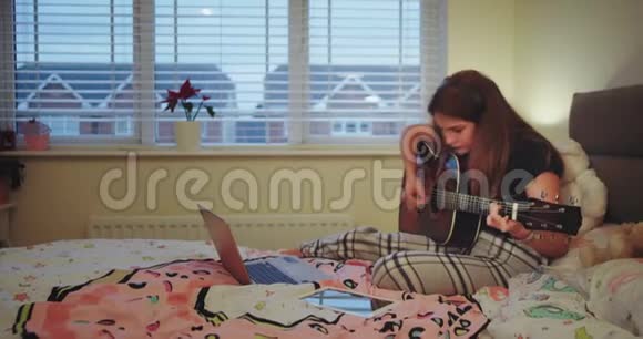 快乐的少年女孩在房间里弹吉他使用耳机她打字时非常集中视频的预览图