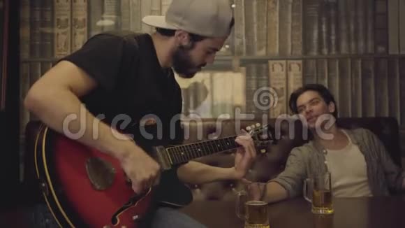 年轻积极的胡须男在酒吧里弹吉他他的男朋友坐在旁边在节奏中摇头视频的预览图