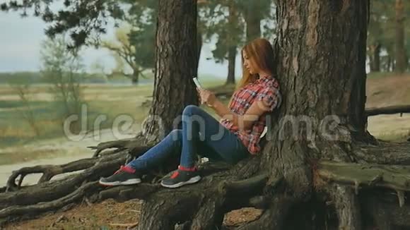 有平板电脑的女孩坐在户外森林里的树上慢动作视频的预览图