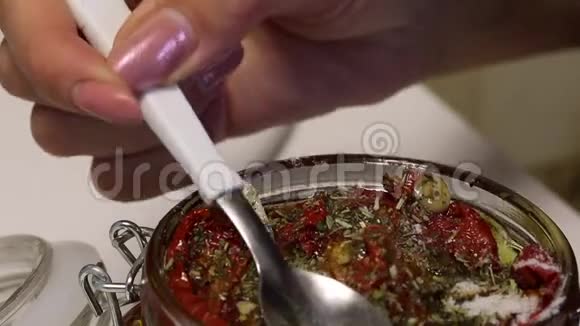 一个女人用干西红柿把勺子伸直它们被堆放在罐子里有一支迷迭香大蒜和香料视频的预览图