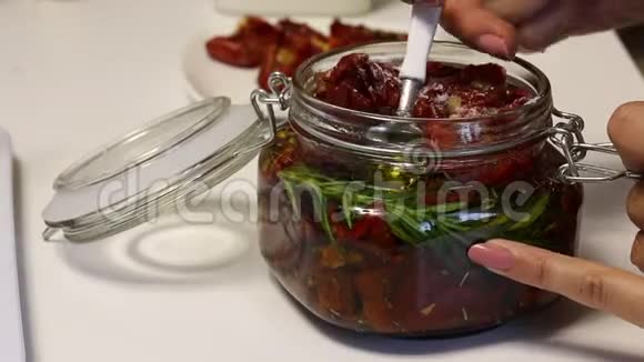 一个女人把一勺干番茄放在罐子里它有迷迭香大蒜和香料的分支涂上橄榄油视频的预览图