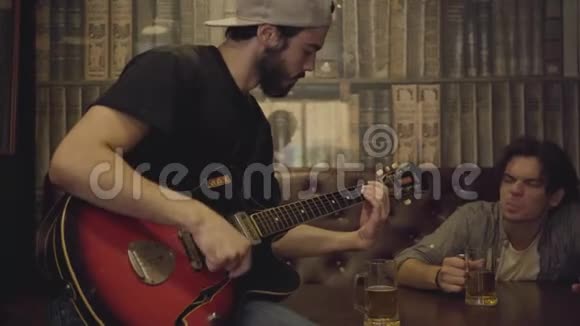 年轻的大胡子男人在酒吧里弹吉他他的朋友坐在旁边按着节奏摇着头在酒吧消遣视频的预览图
