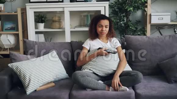 一个迷人的非裔美国女人在电视上悲伤的戏剧后哭泣年轻女士坐在舒适的沙发上视频的预览图
