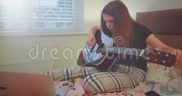 年轻漂亮的女孩开始在卧室里弹吉他她穿着睡衣有一点放松的时间视频的预览图