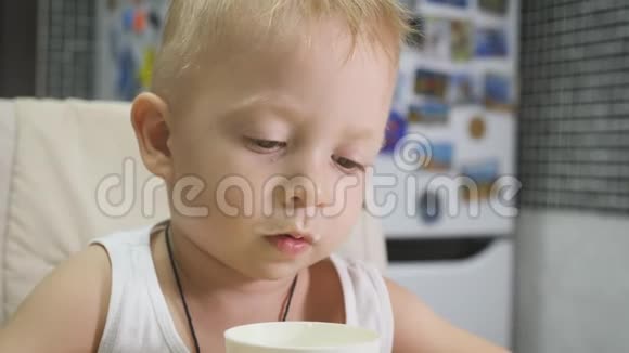 可爱的小男孩在家吃早餐时喝牛奶同时在平板电脑上看卡通儿童和技术视频的预览图