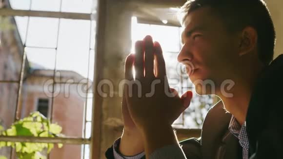 一个年轻人在阳光下祈祷的肖像坐在窗前的一栋老建筑里视频的预览图