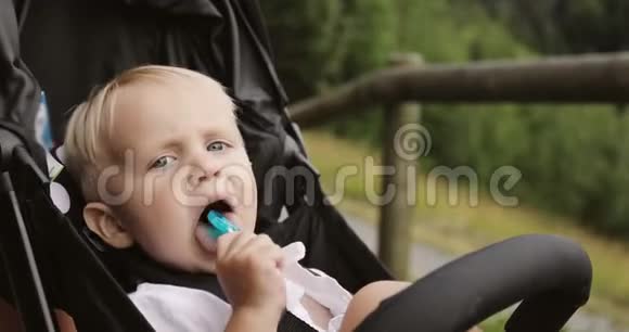 一个可爱的男孩坐在婴儿车厢里吮吸一根棒棒糖视频的预览图