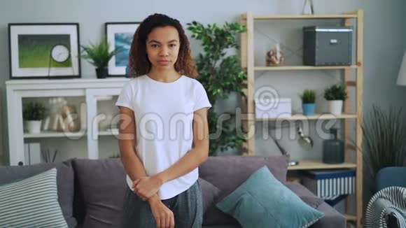 穿着休闲服装的迷人非裔美国女孩站在时尚的现代公寓里的肖像微笑看上去很迷人视频的预览图