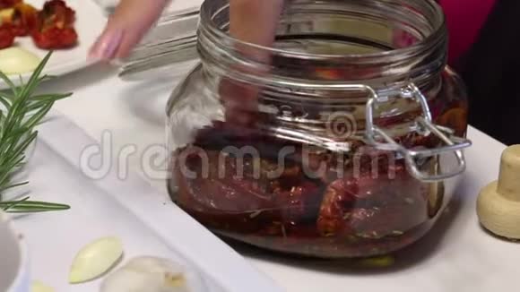 一个女人把干西红柿加到罐子里它有一支迷迭香和香料附近有新鲜的迷迭香西红柿和一个人头视频的预览图