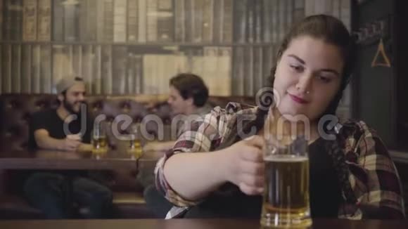 一个梳着辫子的女人坐在酒吧柜台前喝着一杯啤酒两个男人在酒吧喝酒视频的预览图