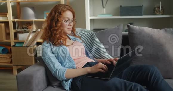 漂亮女人在家里用笔记本电脑在沙发上打字时动作缓慢视频的预览图