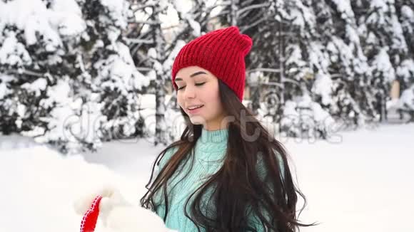 年轻漂亮的女孩穿着一件温暖的蓝色毛衣戴着手套背景是白雪覆盖的树木抱着一颗红色的心视频的预览图