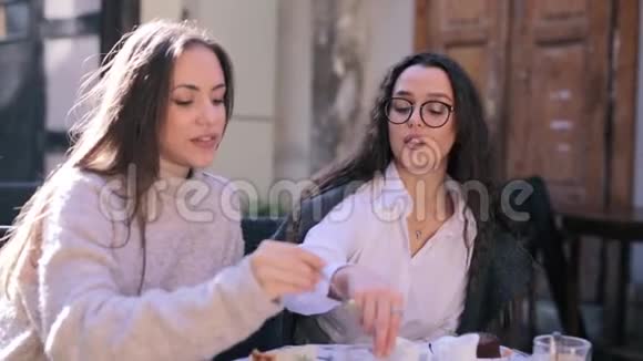 两个漂亮的年轻女人坐在咖啡馆或餐馆的桌子前吃早餐女人倒牛奶给她视频的预览图