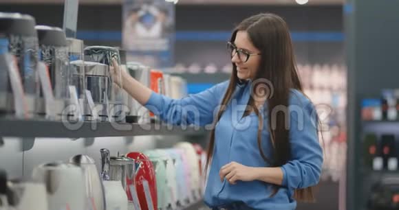 年轻漂亮的黑发女人手里拿着一个电水壶研究价格标签特点和视频的预览图