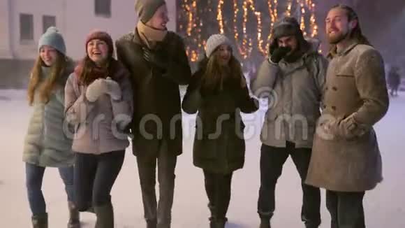 朋友们在大雪纷飞的冬季夜晚在集市上的圣诞市场上散步一群快乐的人视频的预览图