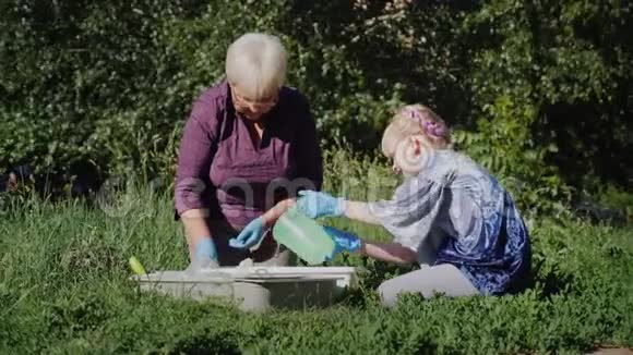 祖母带着孙女把花放在花盆里女孩给地面浇水一只猫在附近散步视频的预览图