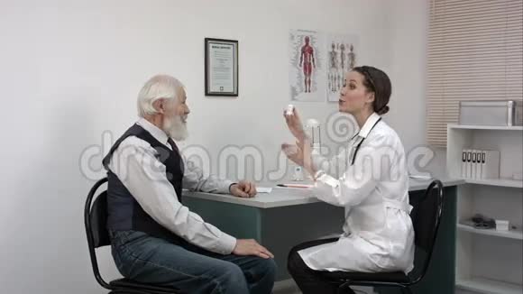 微笑的药剂师拿着一瓶药丸指着老年病人视频的预览图