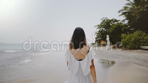 慢镜头跟随年轻美丽的快乐旅游妇女沿着田园风光的热带海洋海滩漫步带着草帽视频的预览图