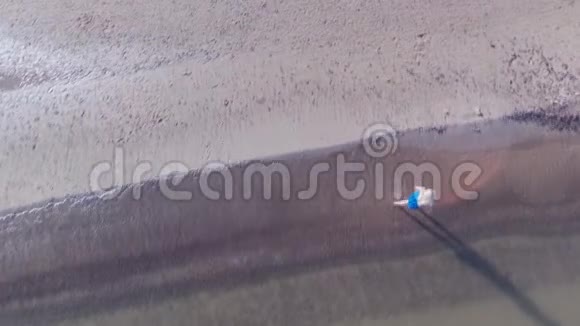 从一个穿着蓝色衣服的金发女郎的飞行无人机在波罗的海海滩上漫步的俯视空中拍摄视频的预览图