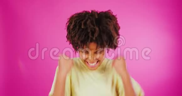 年轻的非裔美国妇女在粉红色的背景下庆祝胜利或成功情感身体语言明亮视频的预览图