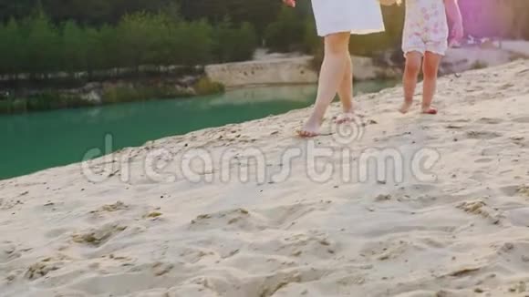 stadicam镜头妈妈牵着一个女儿的手沿着美丽的海滩在湖和森林的背景下视频的预览图