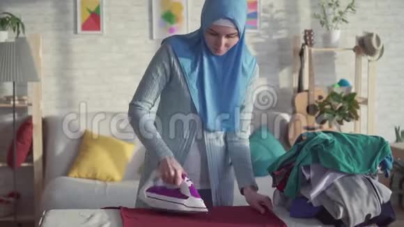 肖像美丽的穆斯林妇女家庭主妇熨亚麻布视频的预览图