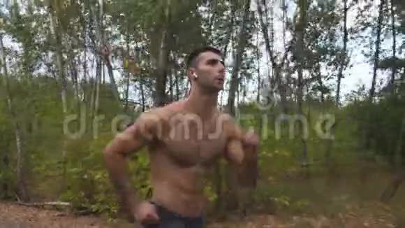 初秋带着无线耳机的英俊的肌肉男在森林附近的小径上快速冲刺运动员视频的预览图