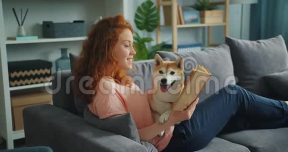 漂亮的学生在公寓里看书微笑着抚摸着可爱的狗视频的预览图