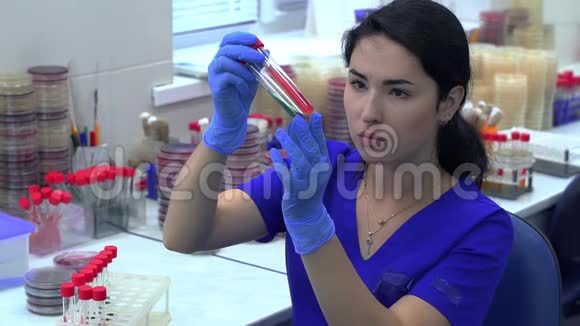 穿蓝色制服的年轻女子从试管架上取两根管子检查液体的颜色和稠度视频的预览图