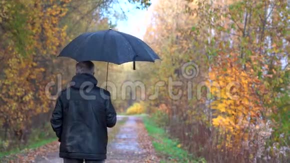 一个身材苗条的男人头发灰白戴着眼镜穿着一件黑色夹克手里拿着一把黑色雨伞走在里面视频的预览图