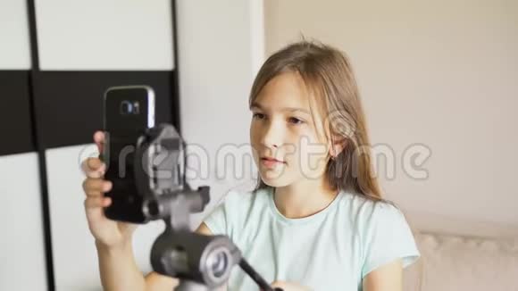 一个年轻女孩在三脚架上安装了一部智能手机用于在线广播女孩描述的是制造广告的设备视频的预览图