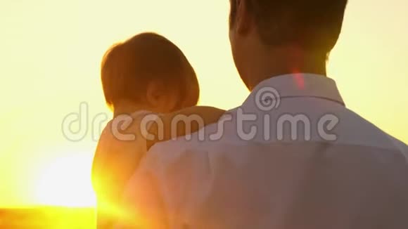 幸福爸爸抱着小女儿抱在阳光的怀里日落时爸爸带着婴儿在草地上散步视频的预览图