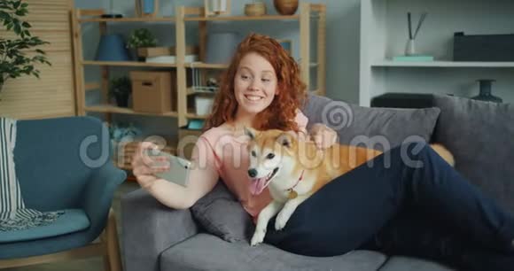 快乐女孩带着丝菲和可爱的狗在沙发上用智能手机摄像头视频的预览图